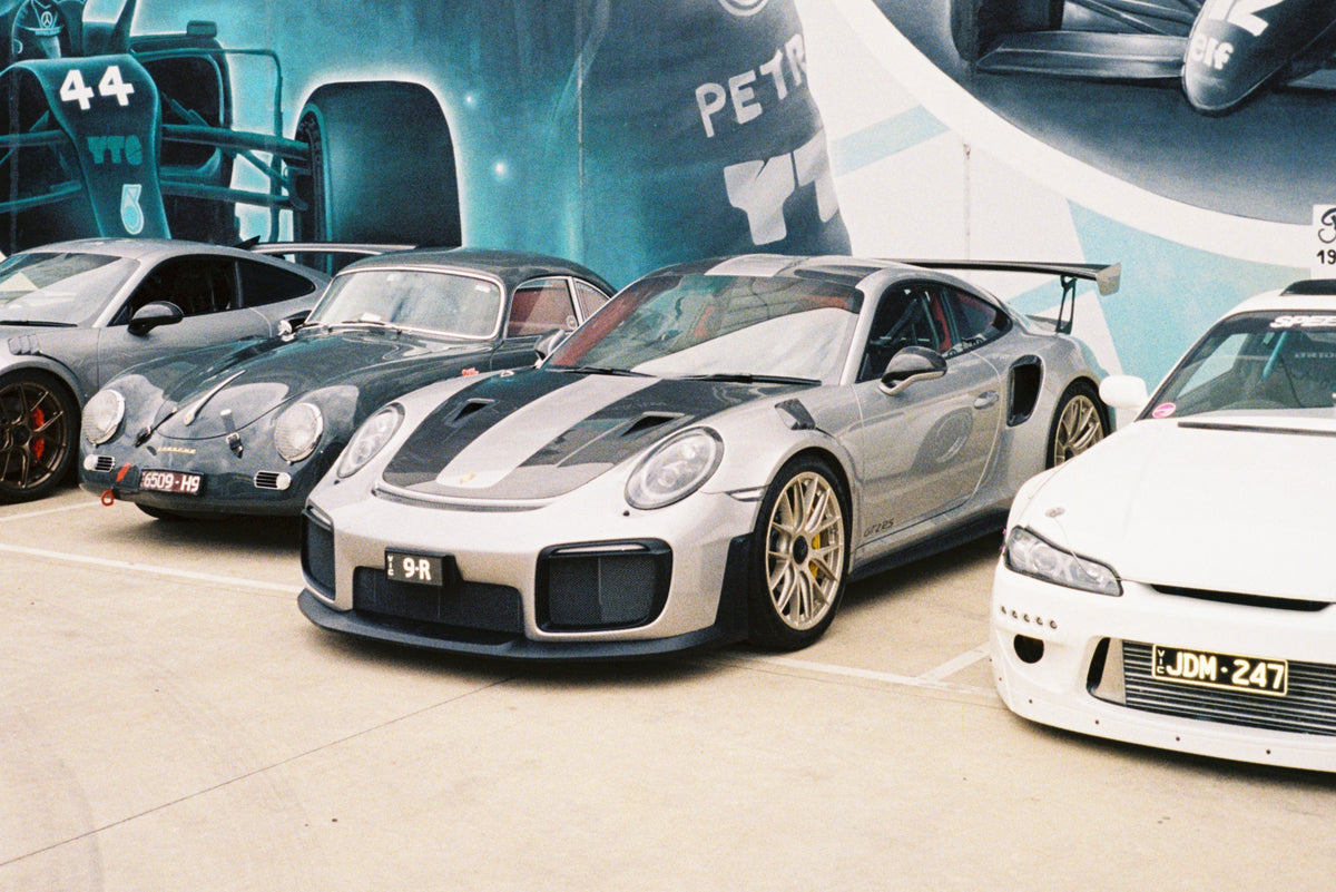 Supercars and Japanese cars parked in-front of a Lewis Hamilton mural