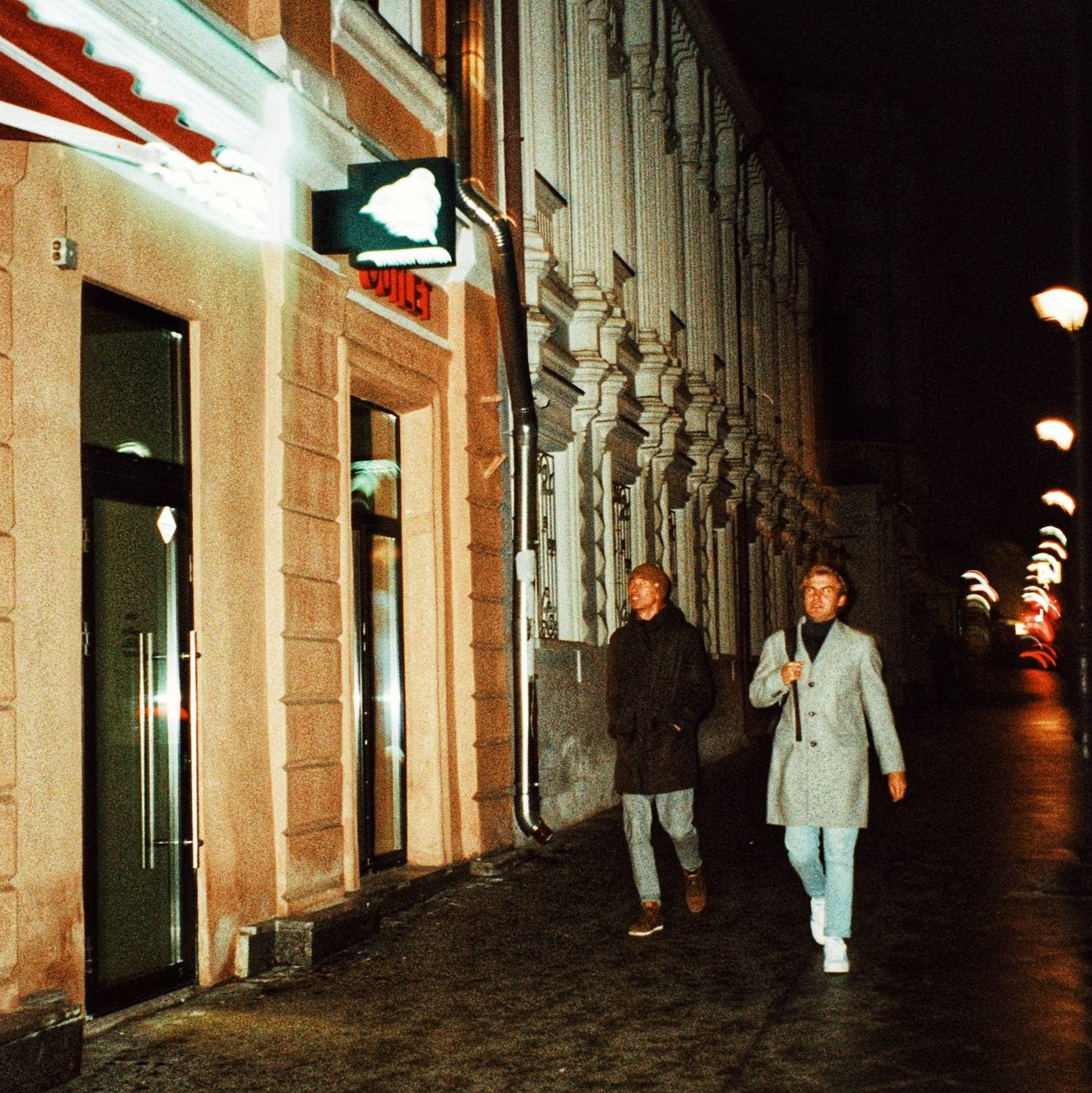 Sample 35mm film photo of two people walking past illuminated buildings at night