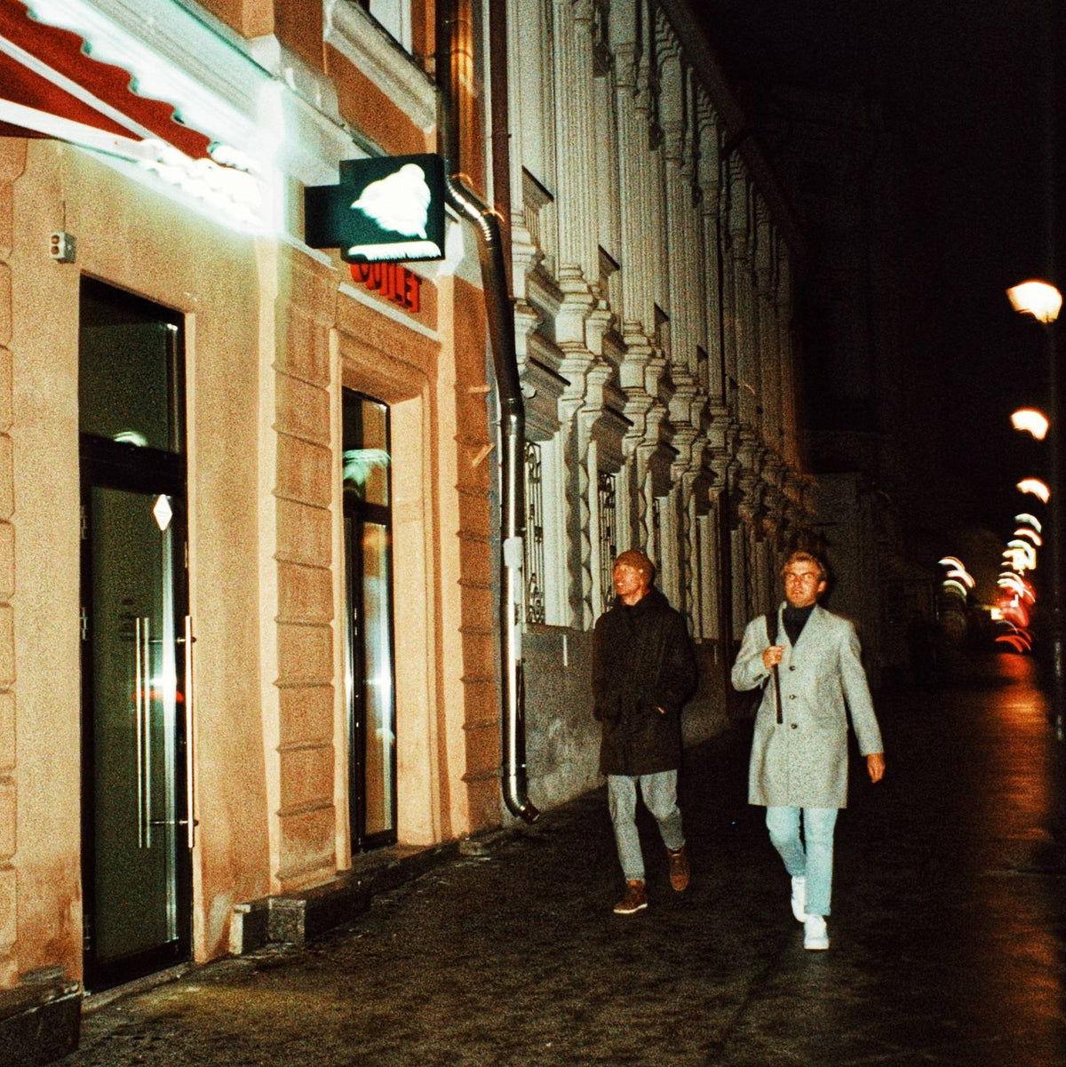 Sample 35mm film photo of two people walking past illuminated buildings at night